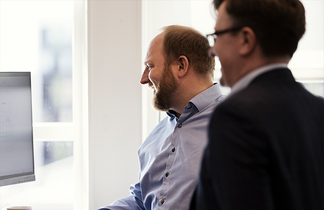 Personer arbetar tillsammans vid dator och digitala system i kontorsmiljö.