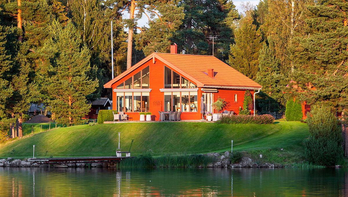 Rött hus med solsken mot sig mitt i ett svenskt landskap.